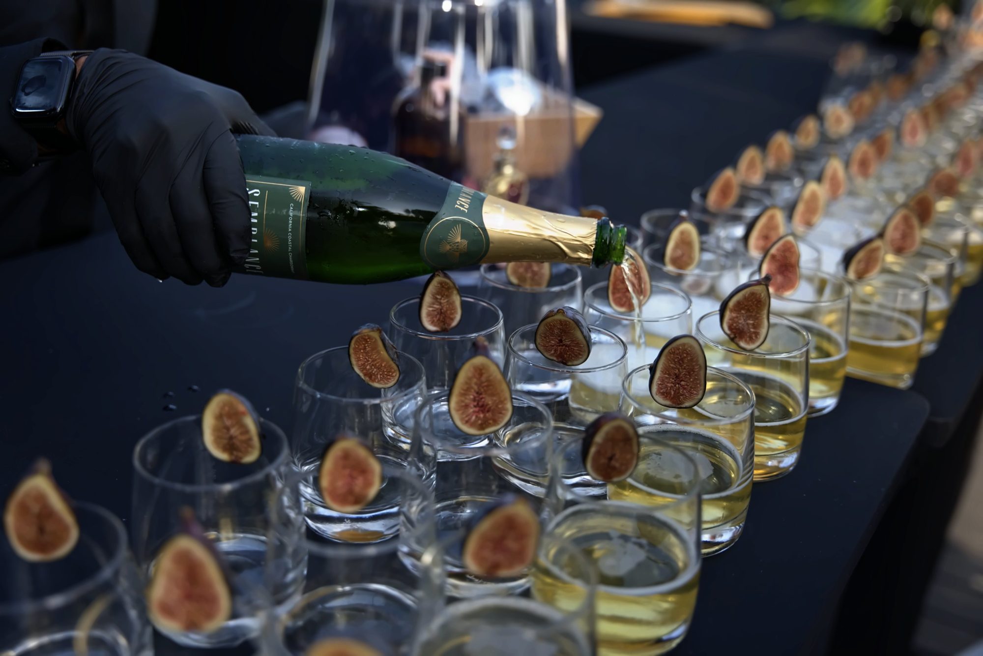 Champagne poured down a long row of glasses garnished with fresh figs