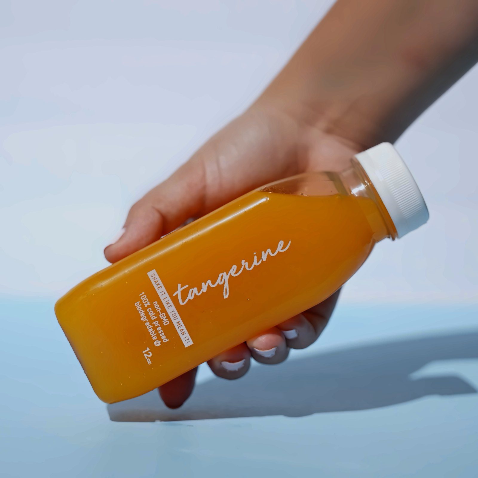 Hand holding a cold-pressed tangerine juice bottle